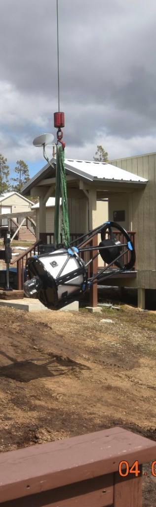 The telescope up in the air attached to a crane being moved towards its building